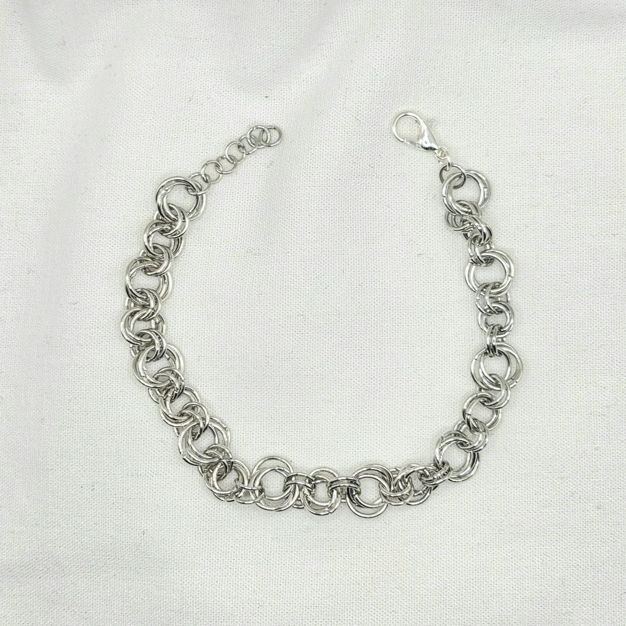 Silver chainmaille bracelet with interlocking rings and lobster clasp on white fabric