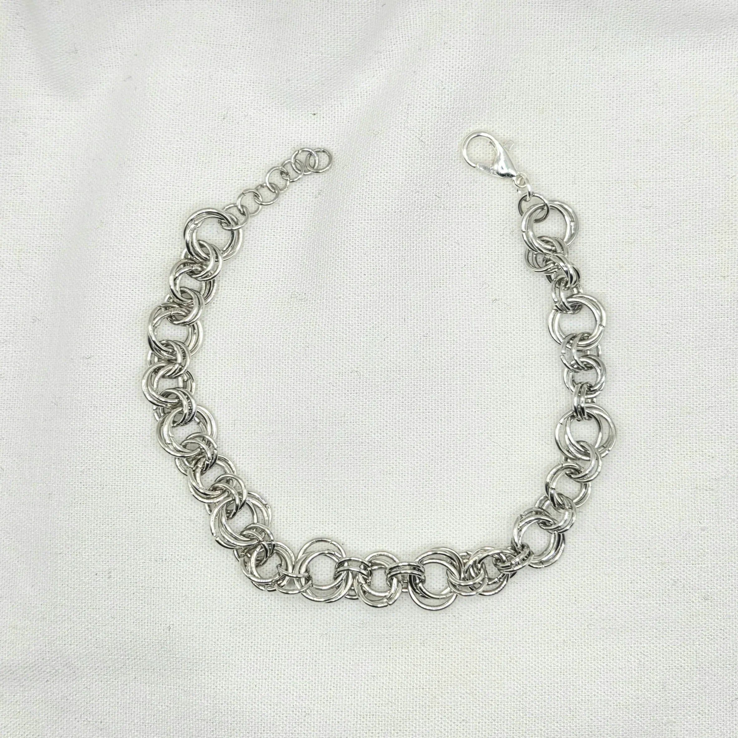 Silver chainmaille bracelet with interlocking rings and lobster clasp on white fabric