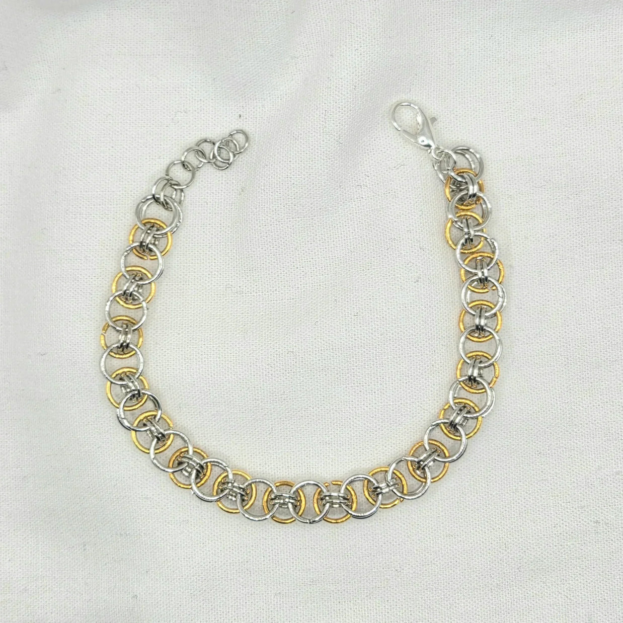 Silver and gold chainmaille bracelet with lobster clasp on white fabric background