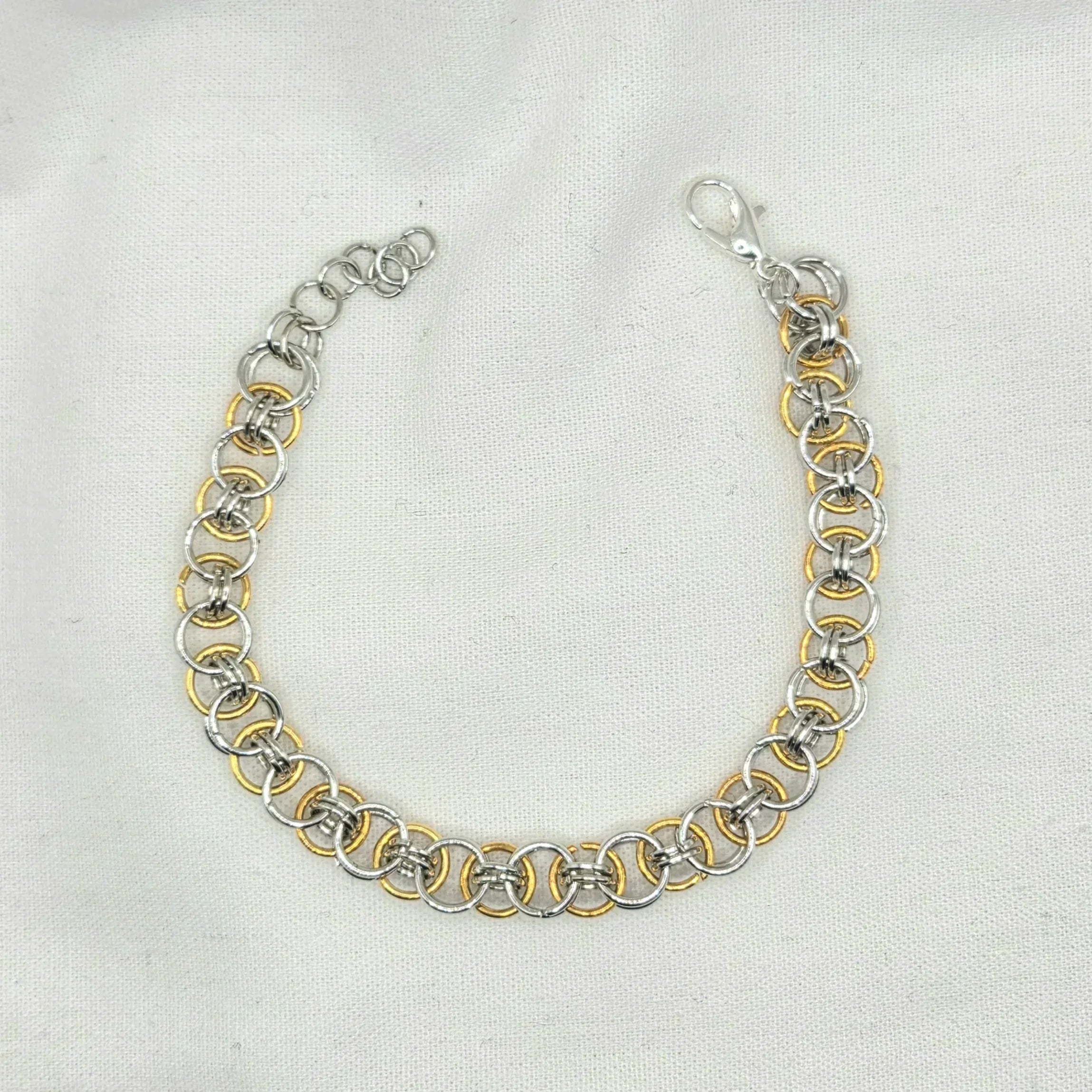 Silver and gold chainmaille bracelet with lobster clasp on white fabric background