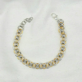 Silver and gold chainmaille bracelet with lobster clasp on white fabric background
