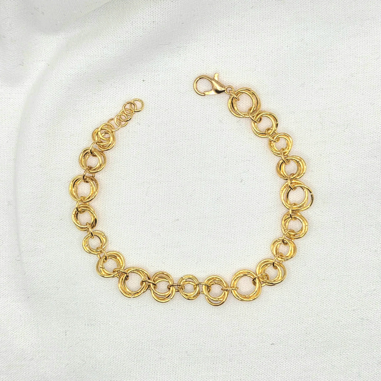 Gold tone interlocking circle chain bracelet with lobster clasp on white fabric background