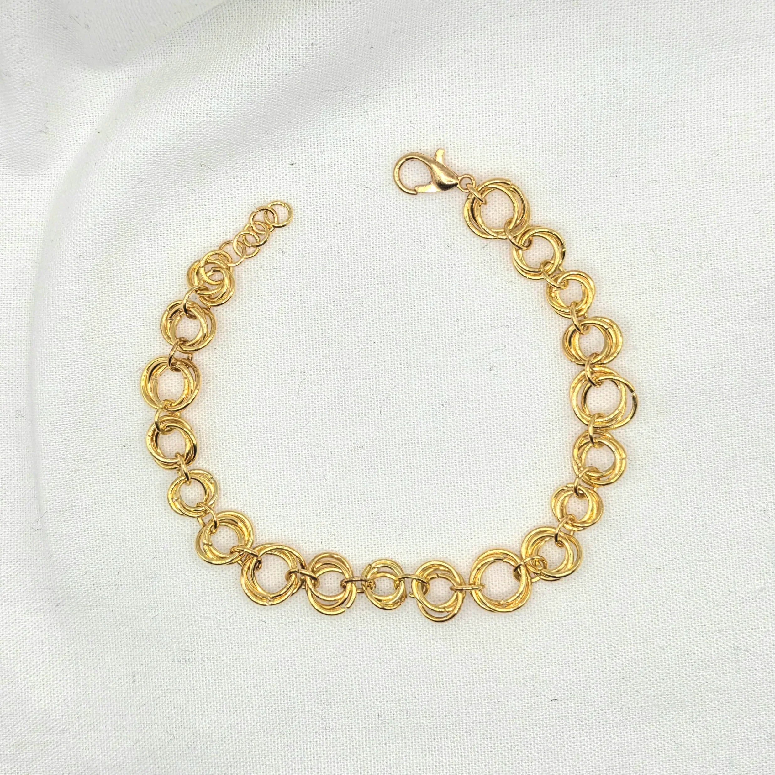 Gold tone interlocking circle chain bracelet with lobster clasp on white fabric background