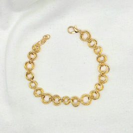 Gold tone interlocking circle chain bracelet with lobster clasp on white fabric background