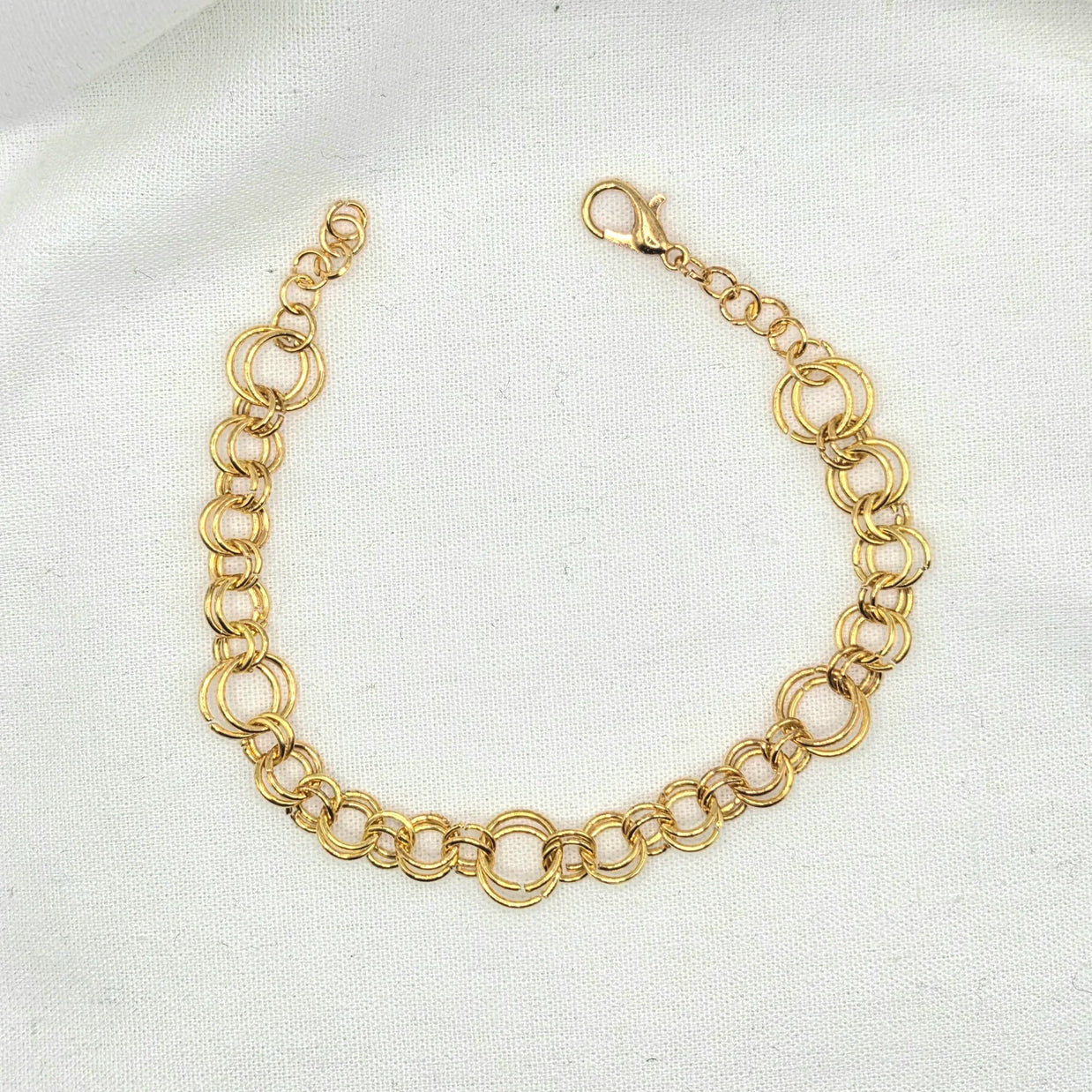 Gold-toned double link chain bracelet with lobster clasp on white fabric background