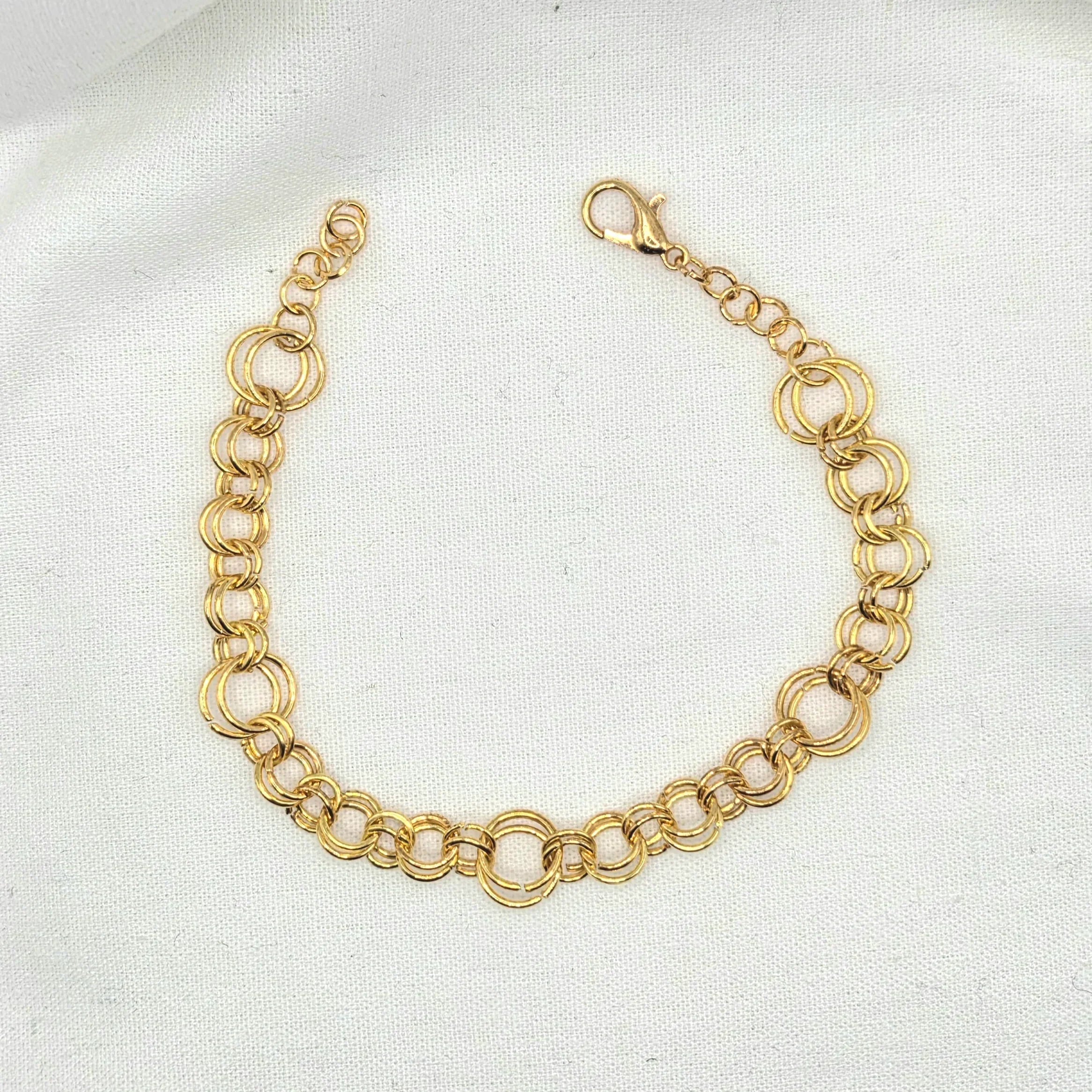 Gold-toned double link chain bracelet with lobster clasp on white fabric background