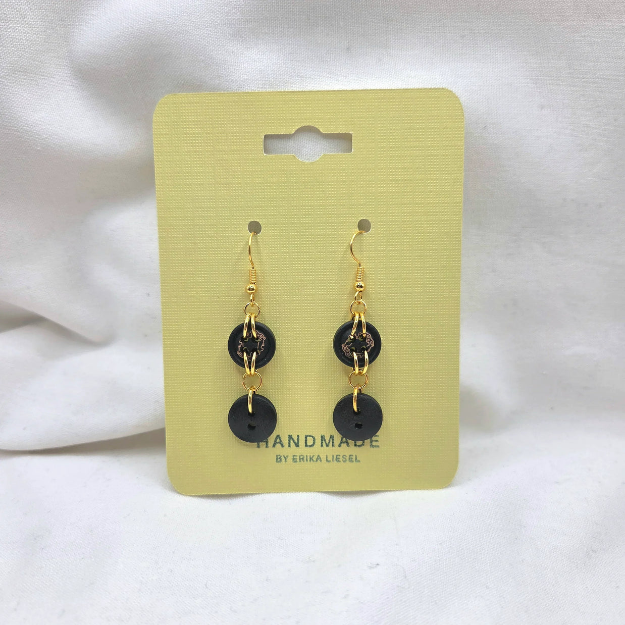 Handmade black button earrings with gold chains on yellow card, cozy crochet gift idea