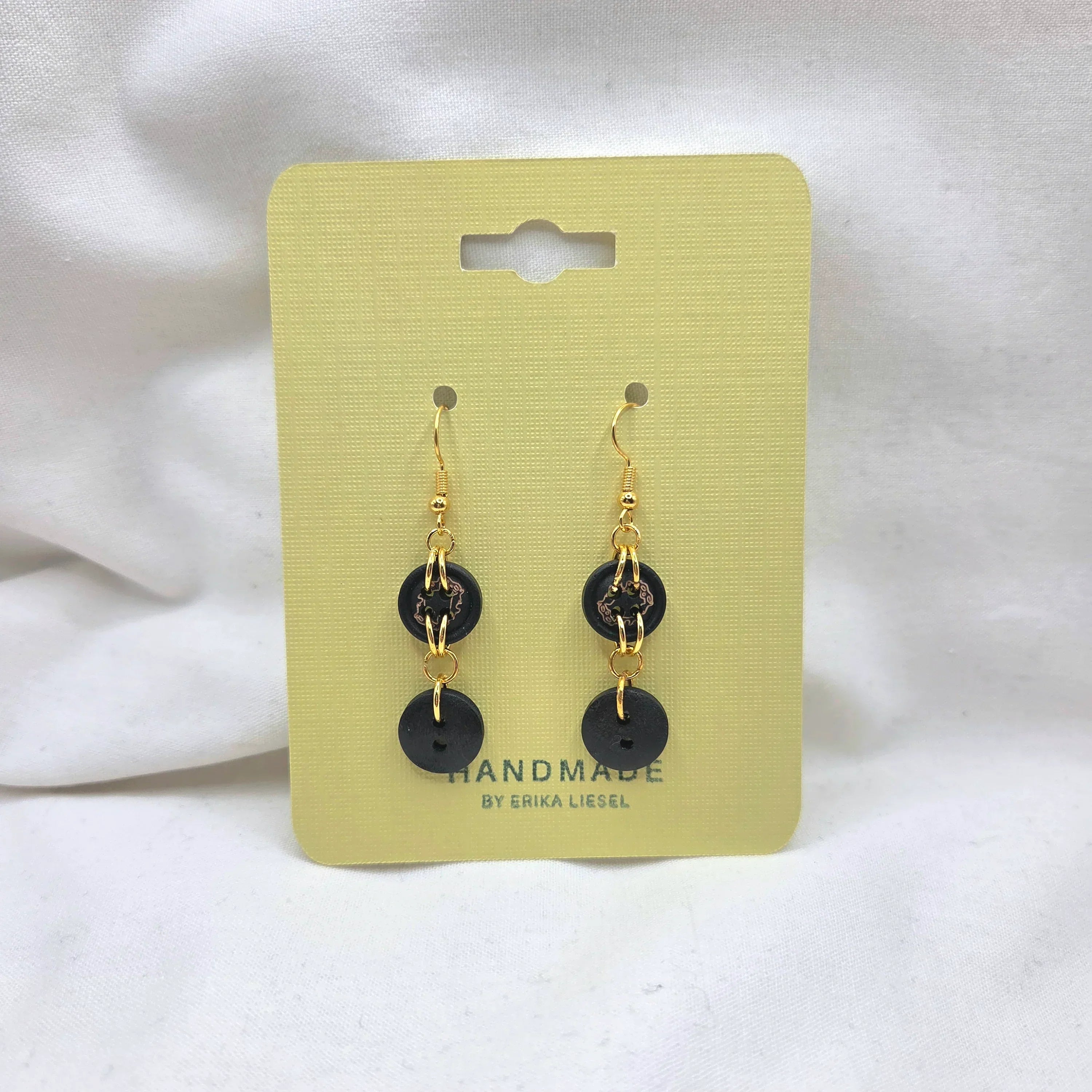 Handmade black button earrings with gold chains on yellow card, cozy crochet gift idea