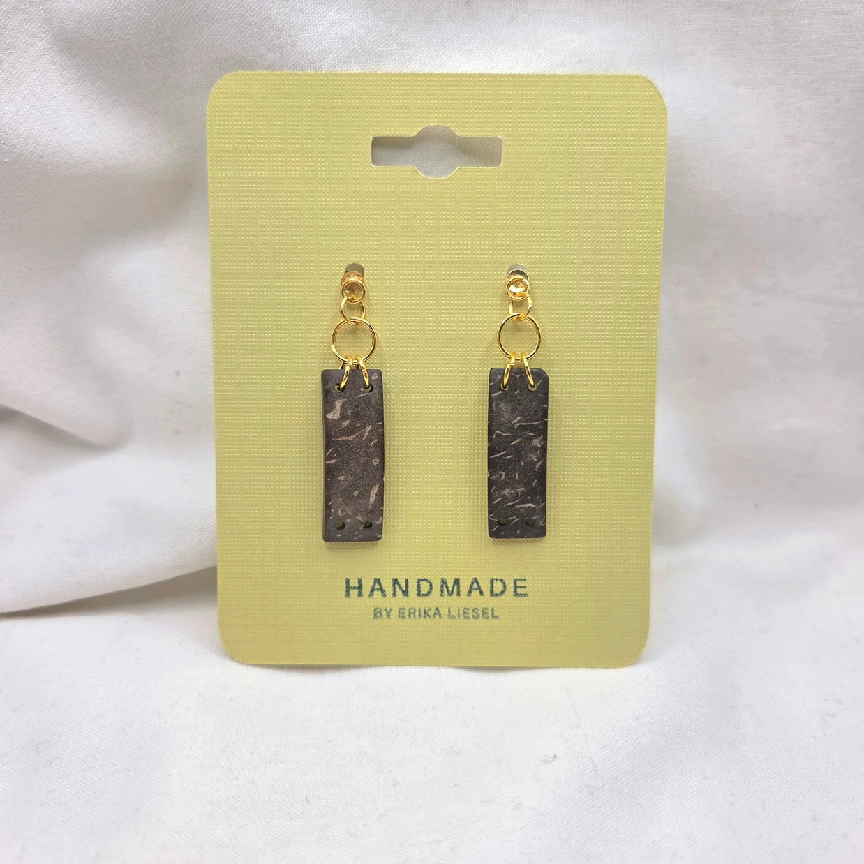 Handmade rectangle dangle earrings with gold hoops and speckled dark charms on yellow card
