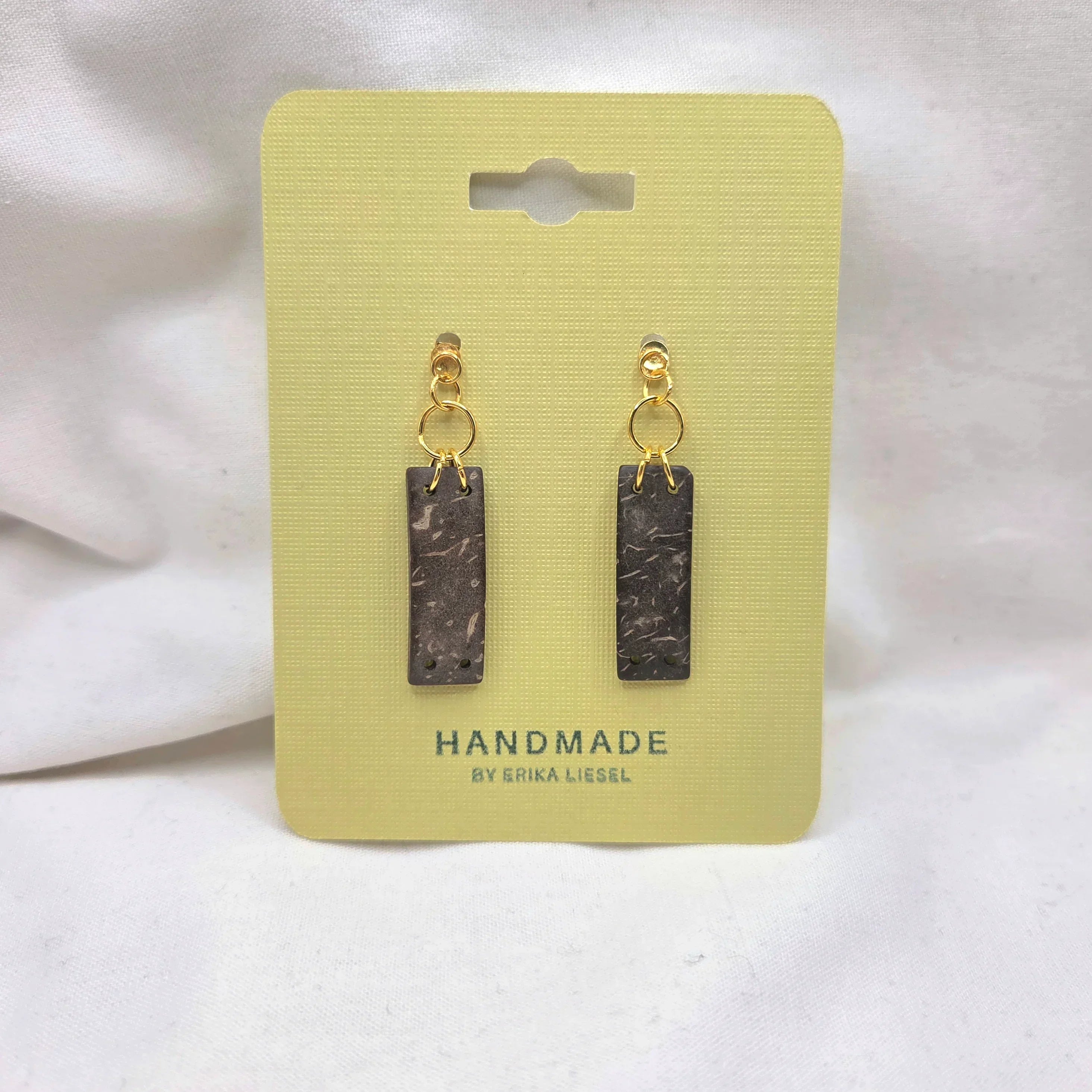 Handmade rectangle dangle earrings with gold hoops and speckled dark charms on yellow card