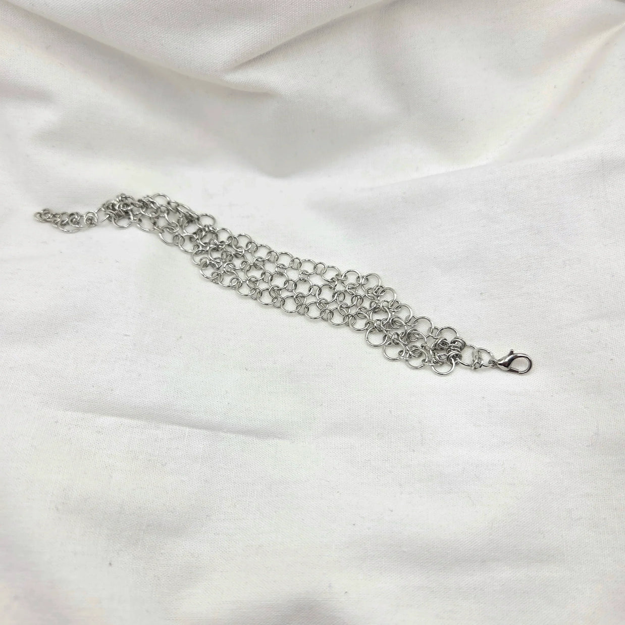 Silver chainmaille bracelet with lobster clasp on white fabric background