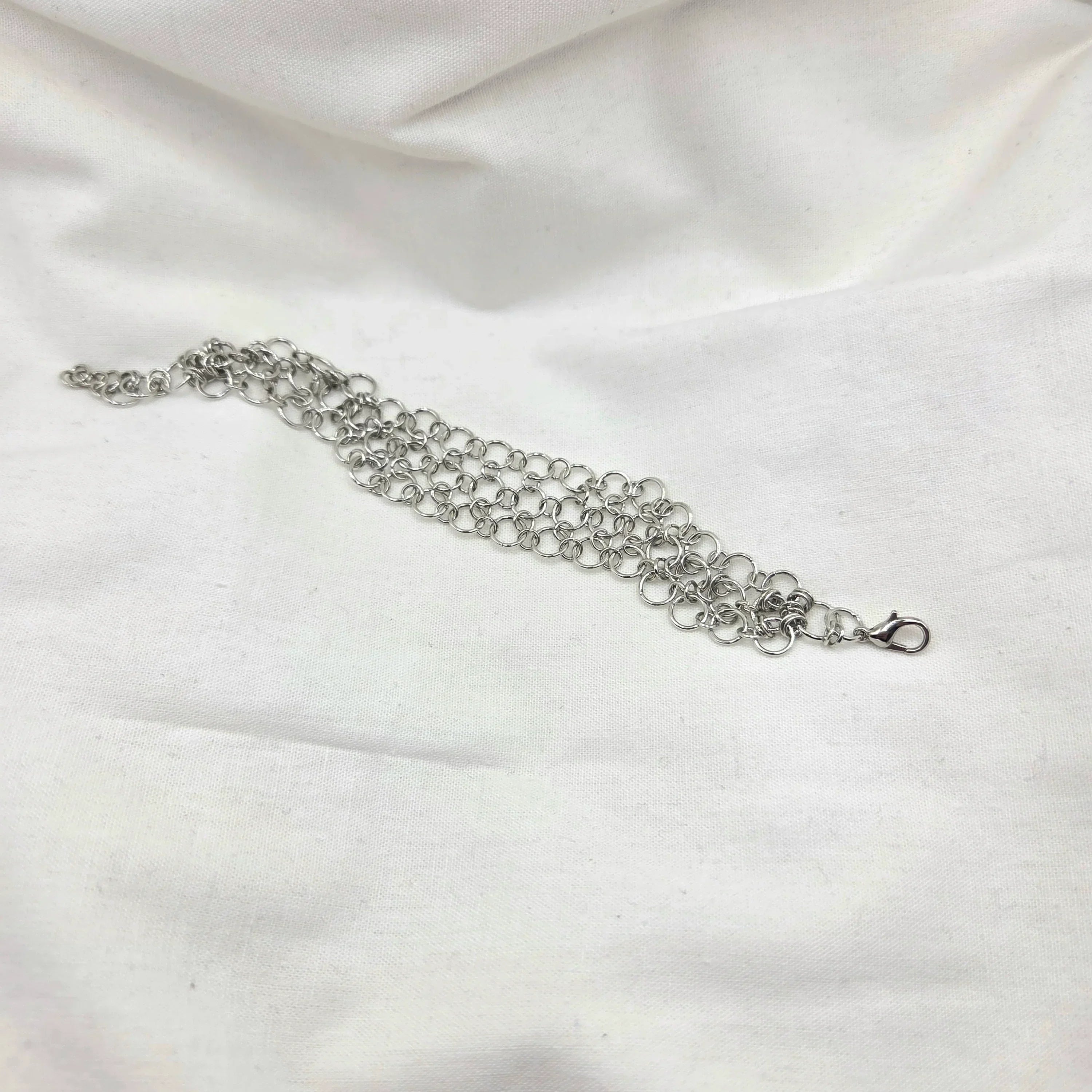 Silver chainmaille bracelet with lobster clasp on white fabric background