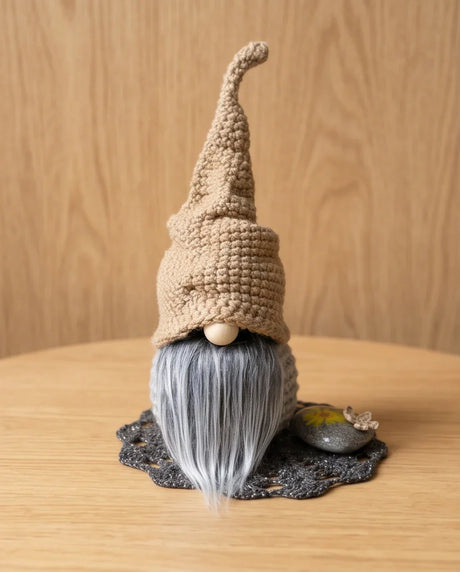 Handmade crochet gnome with gray beard, tan hat, on wooden table — cozy home decor