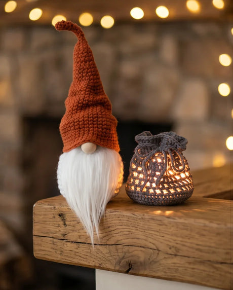 Handmade crochet gnome with white beard and cozy lantern on wooden mantle, warm bokeh lights