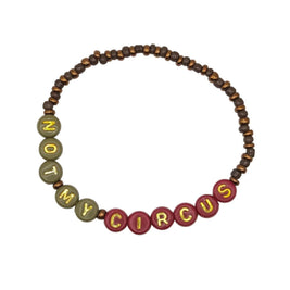 A beaded bracelet on a light gray background, featuring dark brown wooden beads, olive green beads spelling 'NOT', and red beads spelling 'MY CIRCUS' with gold lettering.