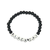 A beaded bracelet composed of glossy black round beads with white letter beads spelling 'BLACKCAT' on a plain light background.