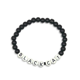 A beaded bracelet composed of glossy black round beads with white letter beads spelling 'BLACKCAT' on a plain light background.