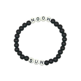 A beaded stretch bracelet on a light gray background, featuring black round beads and white square letter beads spelling 'NOOW SUN'.