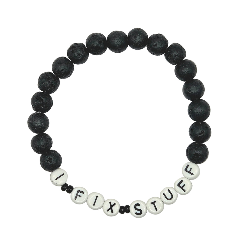 A beaded stretch bracelet on a white background, featuring matte black lava stone beads and white letter beads spelling out 'I FIX STUFF'.