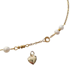 A gold chain necklace featuring small white pearl beads and a polished gold heart-shaped charm, displayed on a light gray background.