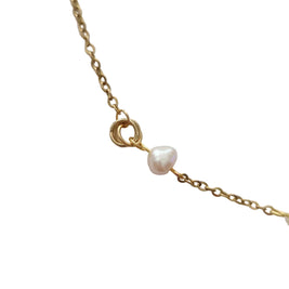 A close-up of a delicate gold chain necklace featuring a small, irregular white freshwater pearl and a triple-ring gold clasp, set against a plain light gray background.
