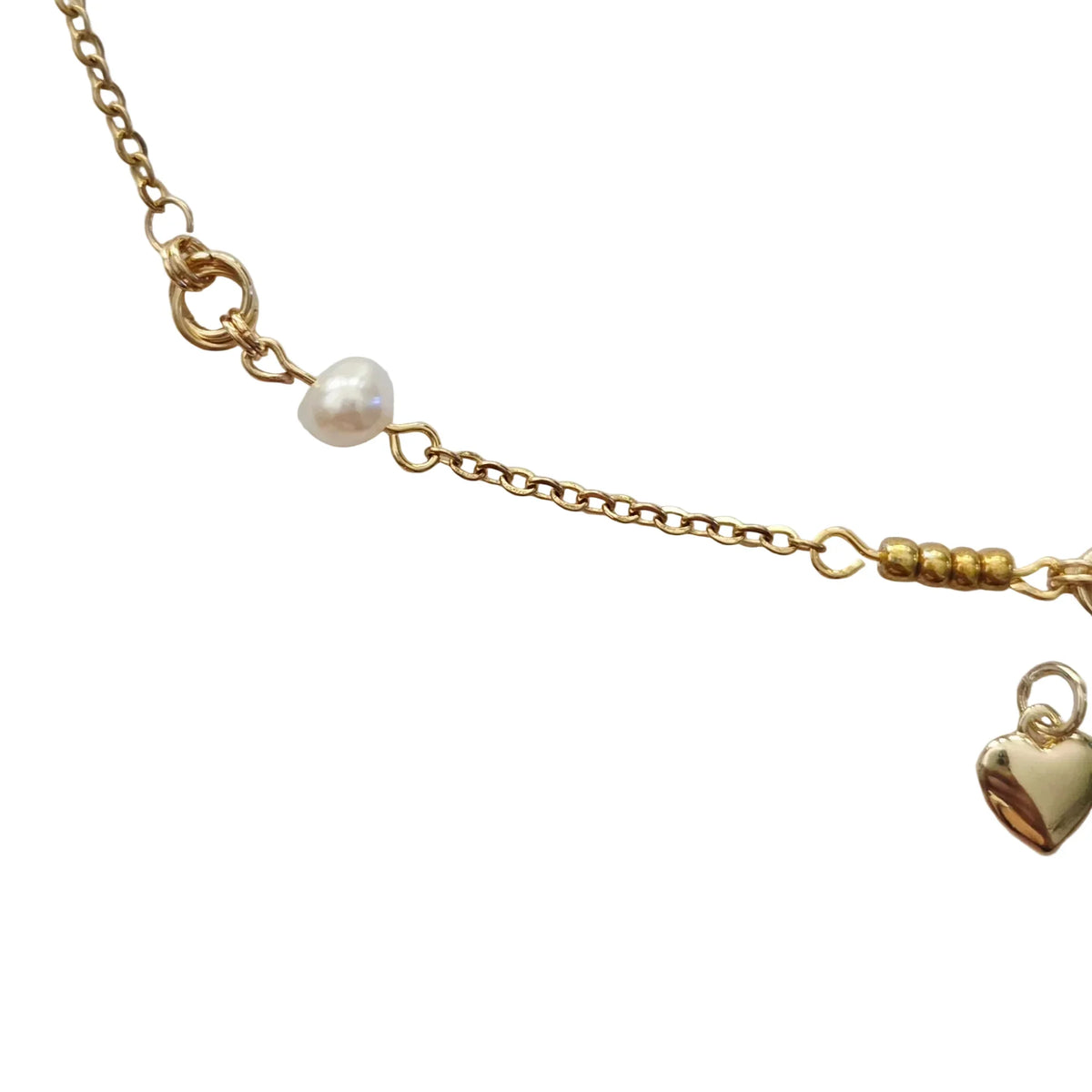 A close-up of a delicate gold chain necklace featuring a small white pearl bead and a polished gold heart charm, displayed on a light gray background.