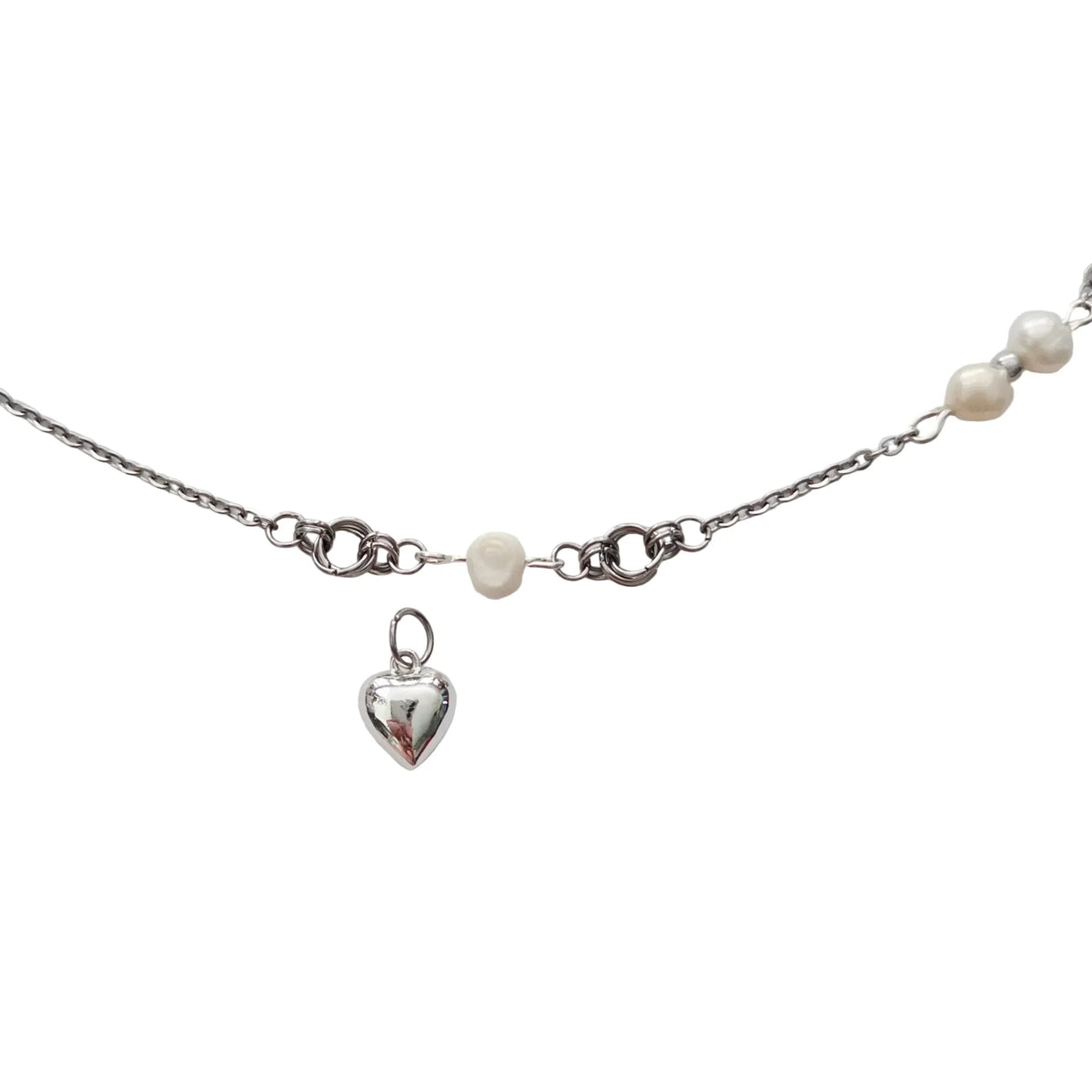A silver chain necklace featuring a small polished heart charm, a white pearl bead, and a row of larger white pearls along the side, displayed on a light gray background.