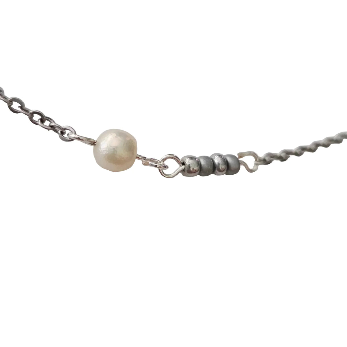A delicate silver chain necklace featuring a single round, lustrous cream-colored pearl and a cluster of small metallic beads, shown on a plain light gray background.