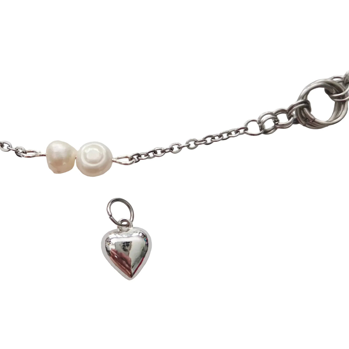 A silver chain bracelet featuring two small white pearl beads and a dangling polished silver heart charm, shown on a plain light gray background.