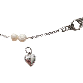 A silver chain bracelet featuring two small white pearl beads and a dangling polished silver heart charm, shown on a plain light gray background.