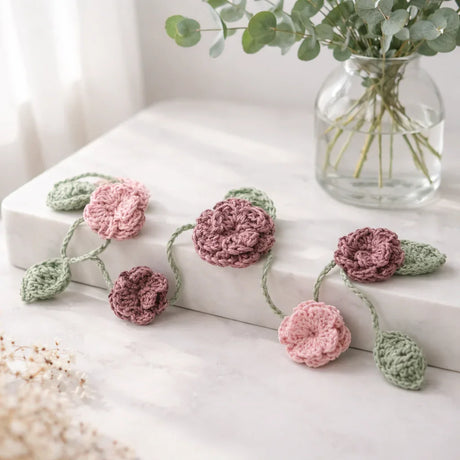 Handmade crochet flower garland with pink and green blooms on marble, perfect for cozy home decor