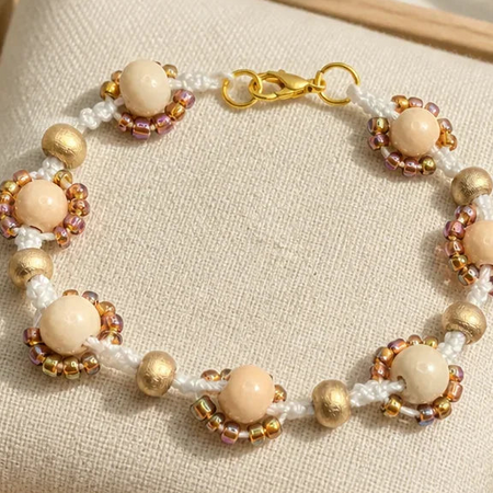 Handmade crochet beaded bracelet with cream pearls, gold beads, and white cord on fabric display