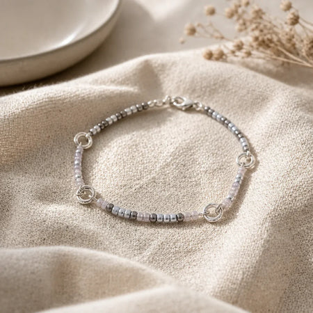 Delicate beaded bracelet with silver and pink beads, styled on soft fabric for cozy, handmade charm.