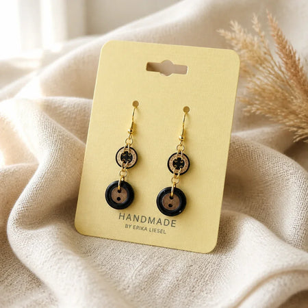 Handmade button earrings with gold hooks on cream card, cozy fabric background