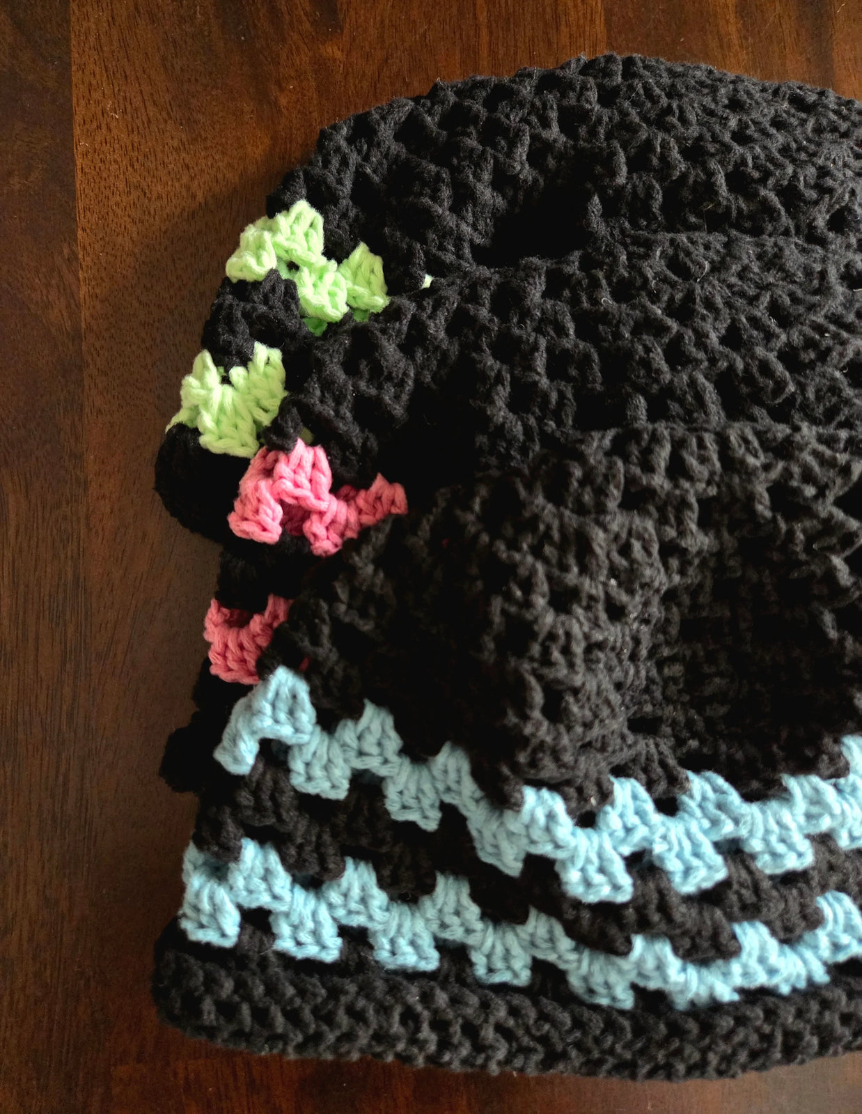 Stack of handmade black crochet hats with green, pink, and blue accent stripes on wood table