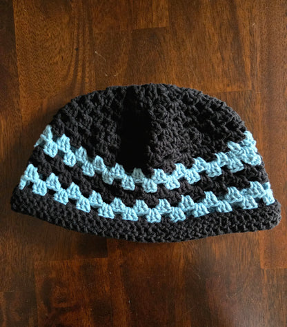 Handmade crochet beanie hat with black and blue stripes on a wooden table