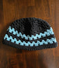 Handmade crochet beanie hat with black and blue stripes on a wooden table