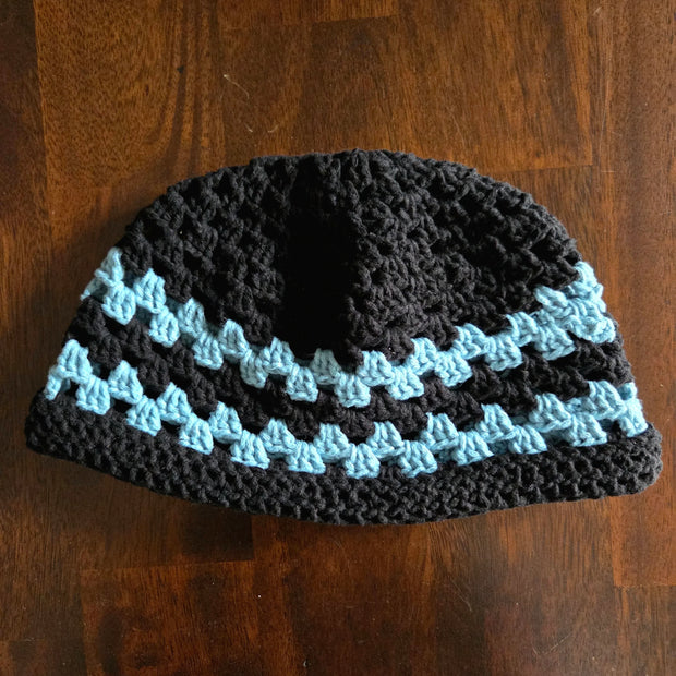 Handmade crochet beanie hat with black and blue stripes on a wooden table