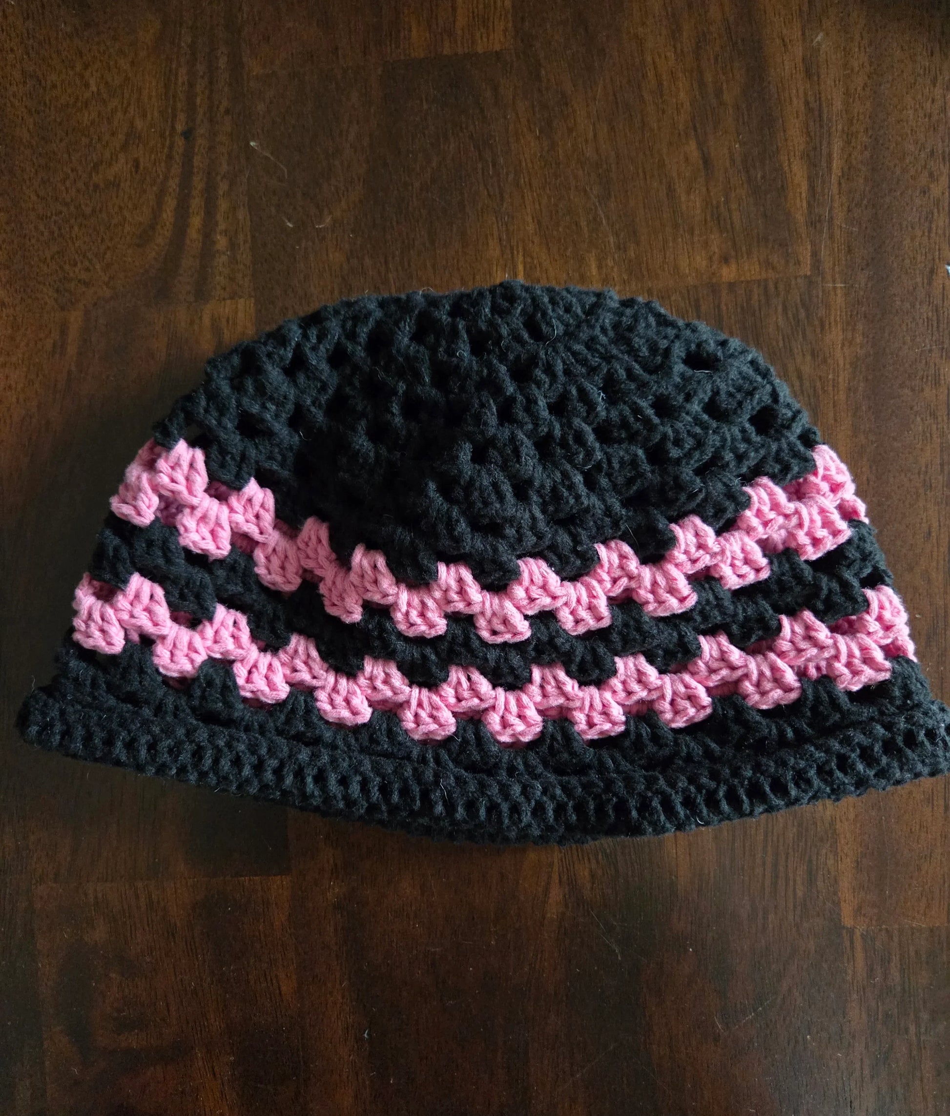 Handmade crochet beanie hat with black and pink stripes on a wooden table
