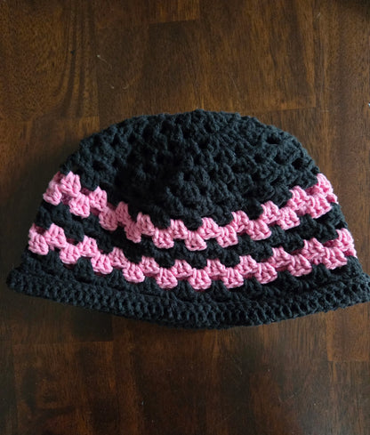 Handmade crochet beanie hat with black and pink stripes on a wooden table