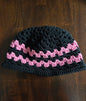 Handmade crochet beanie hat with black and pink stripes on a wooden table