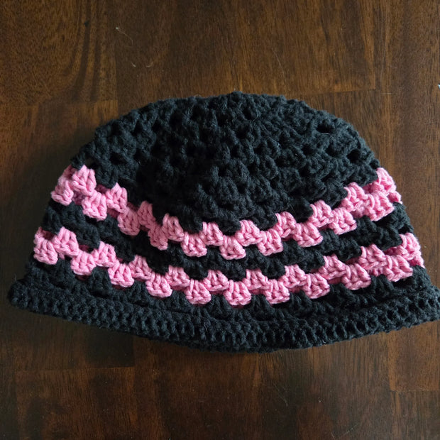 Handmade crochet beanie hat with black and pink stripes on a wooden table