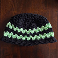 Handmade crochet beanie with black and green stripes on a wood surface.
