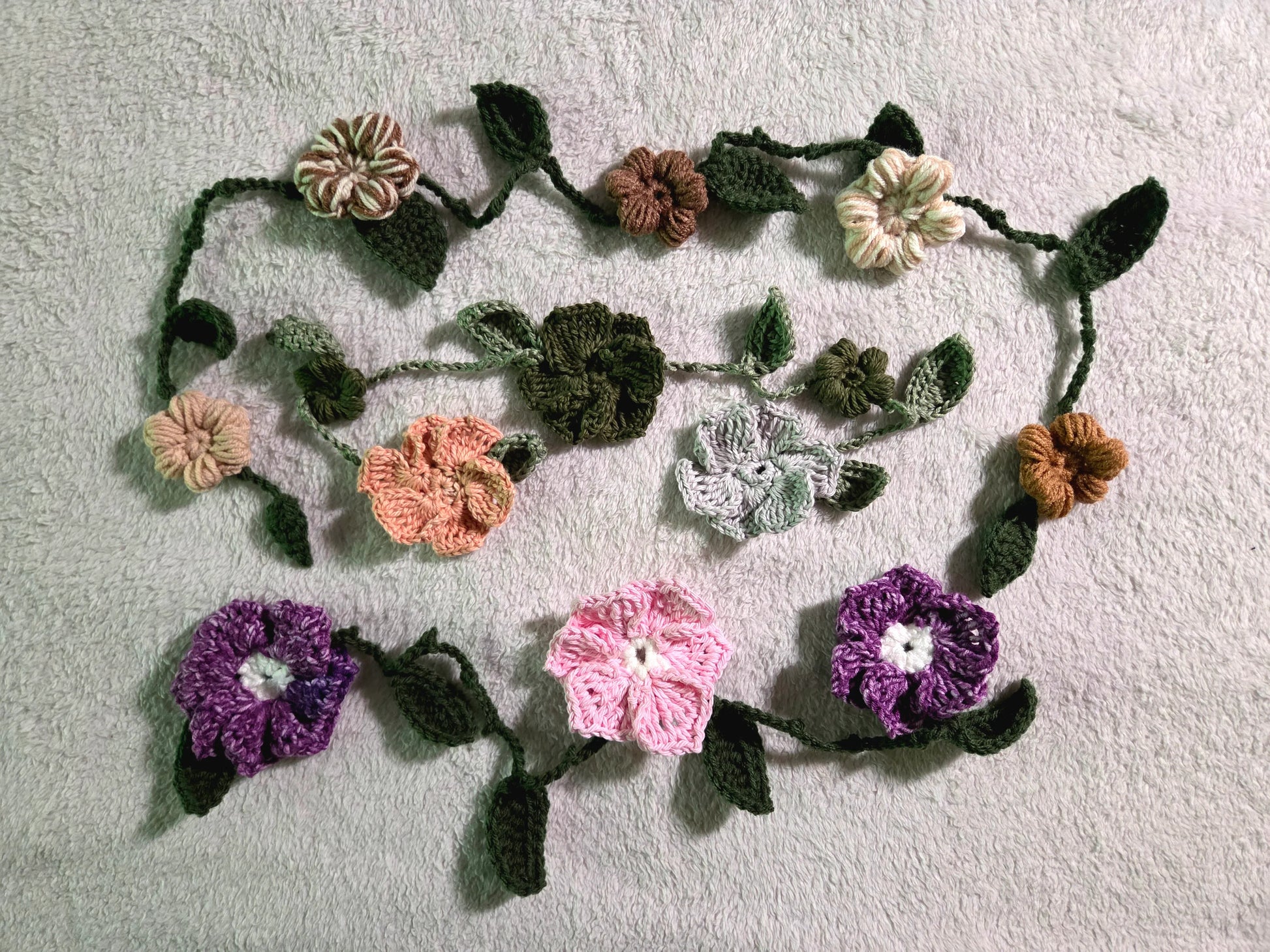 Handmade crochet flower garland with green leaves on light gray textured fabric background