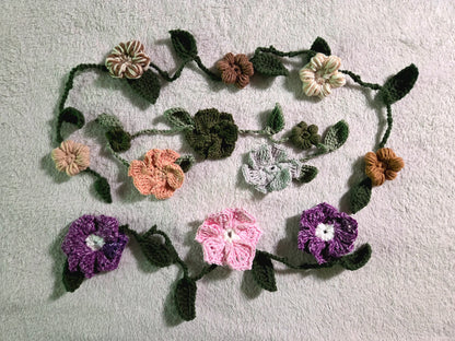 Handmade crochet flower garland with green leaves on light gray textured fabric background