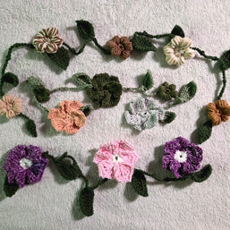 Handmade crochet flower garland with green leaves on light gray textured fabric background