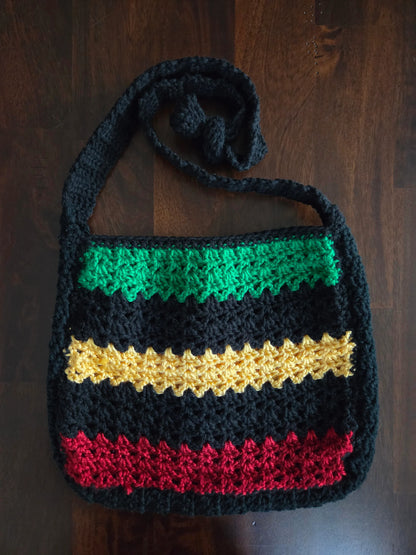 Handmade crochet bag with green, yellow, red, and black stripes on wooden background