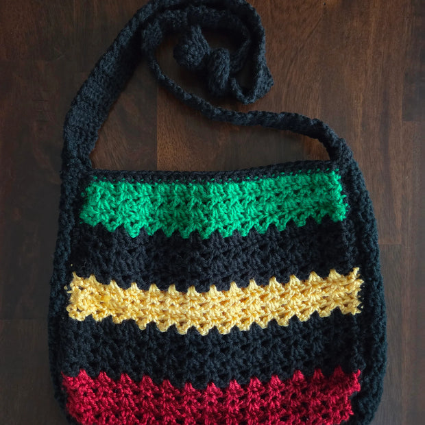 Handmade crochet bag with green, yellow, red, and black stripes on wooden background