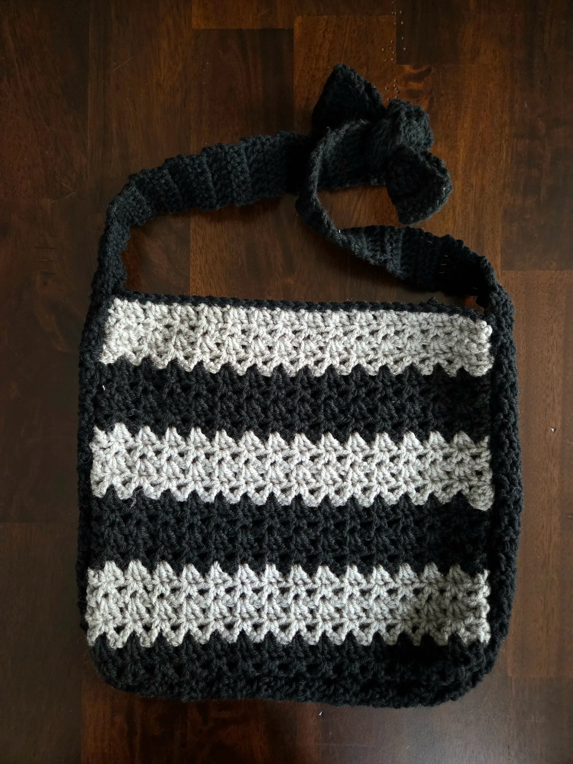 Handmade crochet bag with black and gray stripes and a bow on the strap on a wood surface