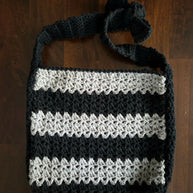 Handmade crochet bag with black and gray stripes and a bow on the strap on a wood surface